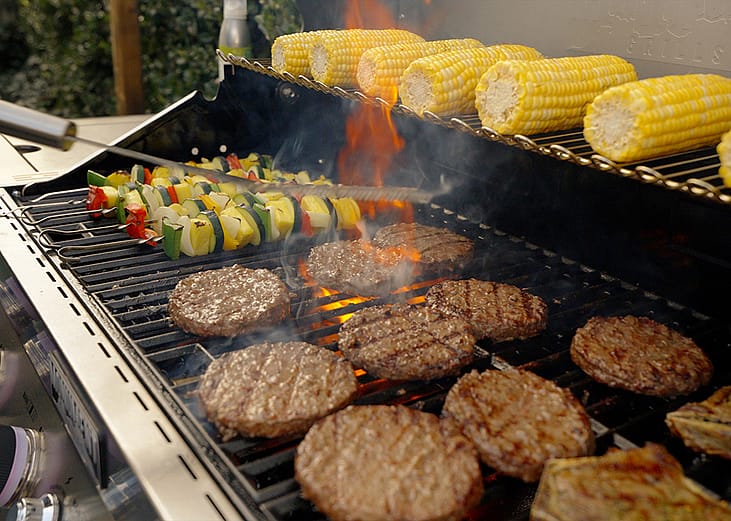 An outdoor gas grill cooking and warming food over flames. 