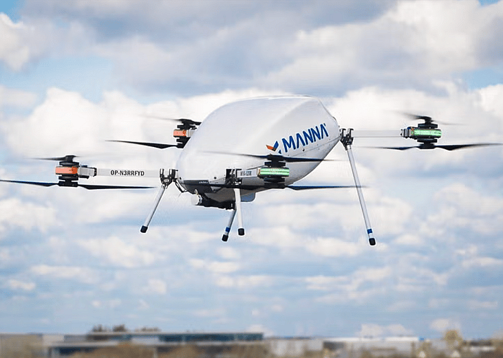 A Manna Air Delivery drone in action in the sky with clouds in the background.