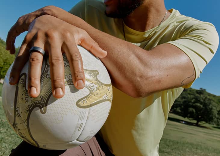A person wearing a smart sleep ring while holding a ball outdoors.