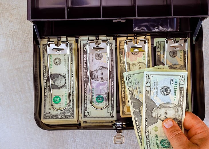 US banknotes neatly organized inside a metal cash box.