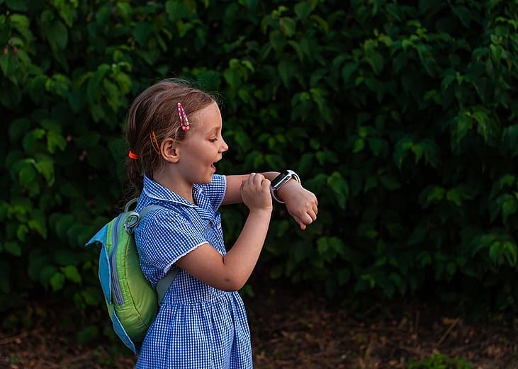 A school kid using her smartwatch outdoors in a park.