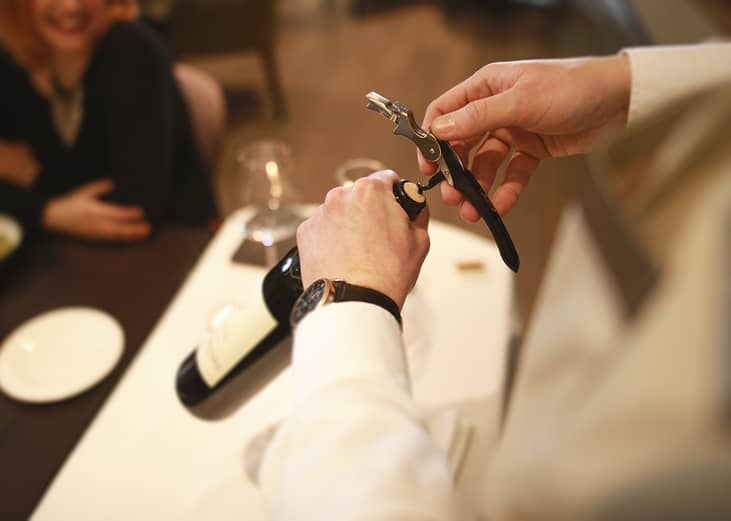 A professional waiter opening a wine bottle with a corkscrew.