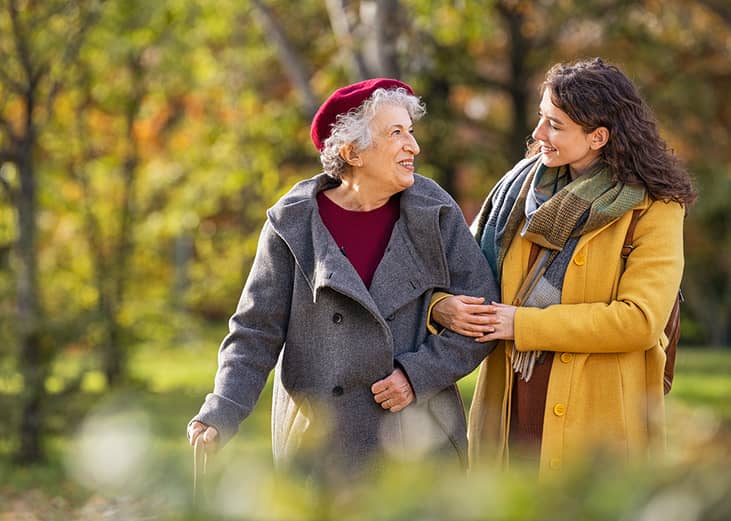 A young woman with her senior grandmother happily walking together at a park.