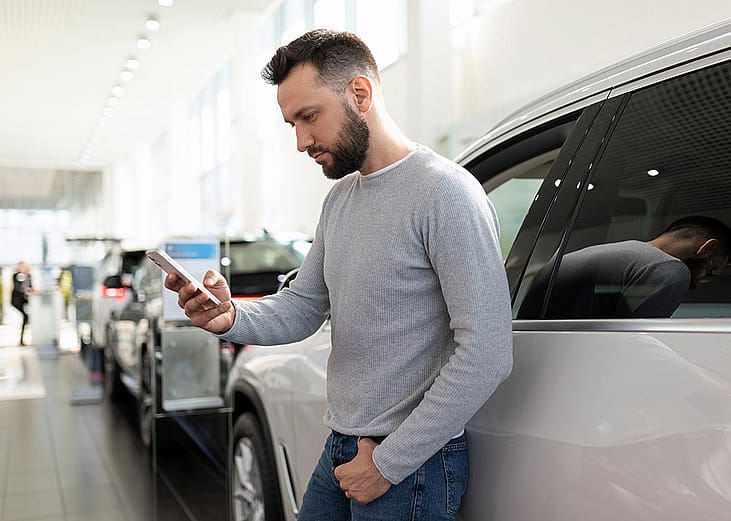 A man at a car dealership looking at information on his phone.