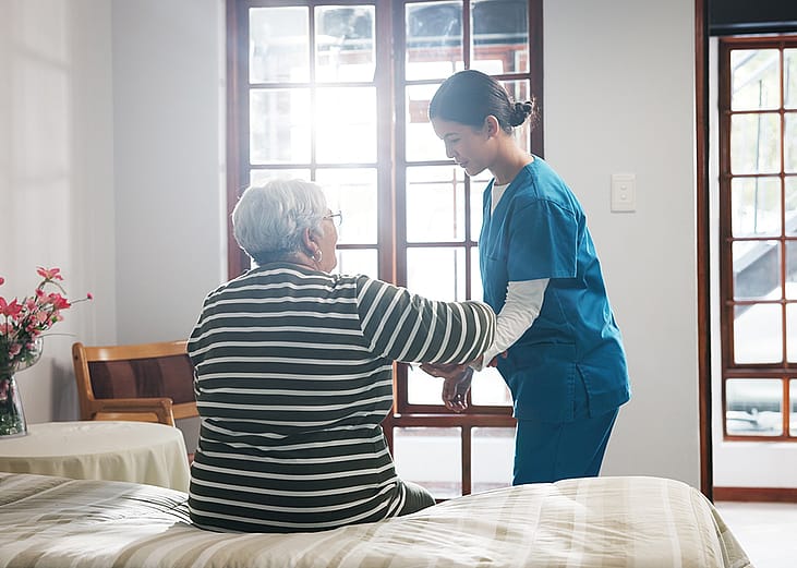 A home nurse assisting an elderly patient from the bed in the morning.
