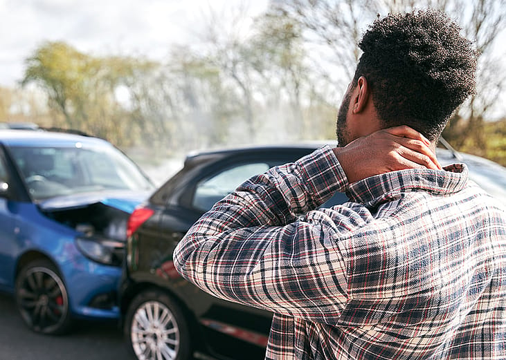 A stressed young man looking at the damage his car caught after an accident.