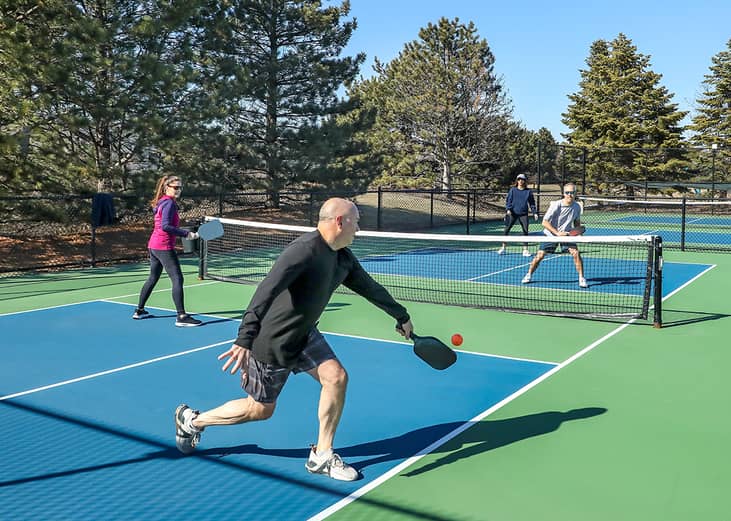 A player hitting a backhand stroke during a pickleball doubles game in spring.
