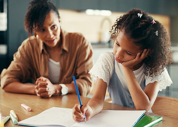 A mother supporting her young daughter with ADHD in answering a learning exercise at home.