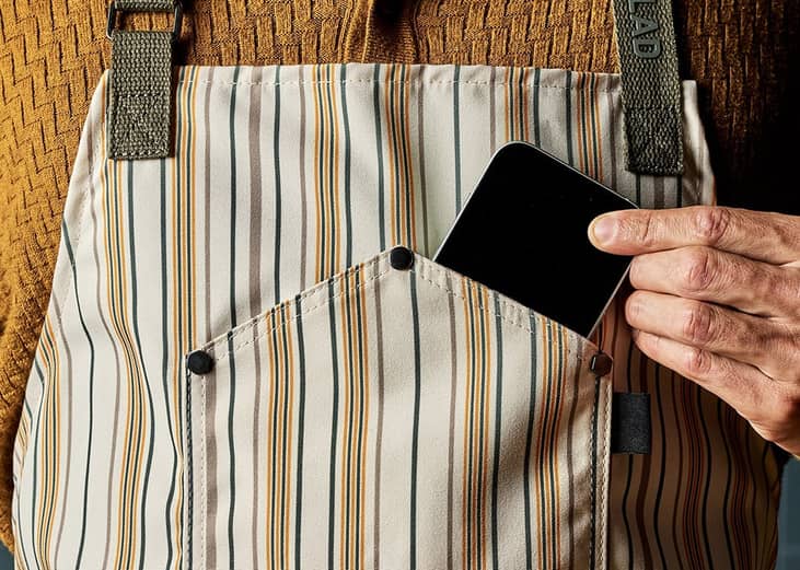 A person putting a smartphone inside an eco-friendly and modern apron's phone pocket.