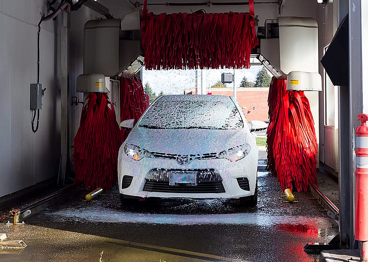 A white car covered in soap suds as it passes through a car wash lane.