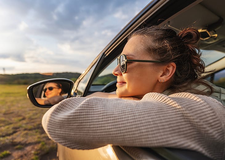 A happy young woman leaning out of a car window during a ride.