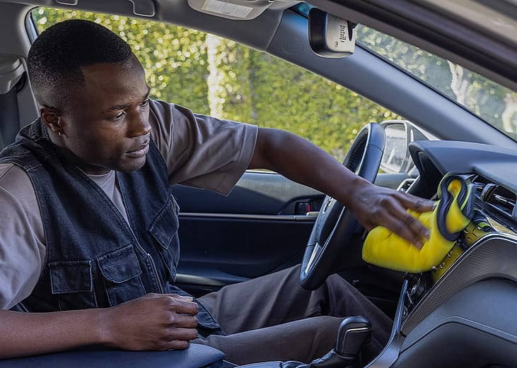 A person cleaning a car's dashboard and console using a microfiber cloth.