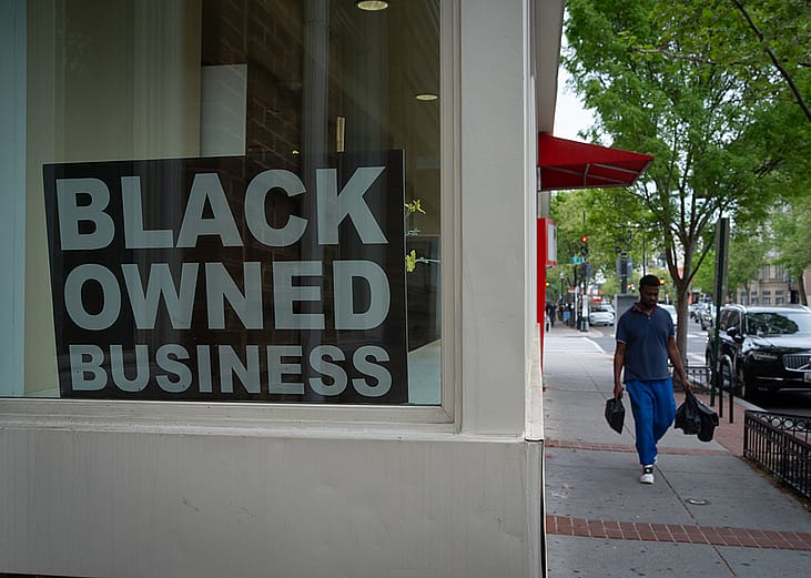 A Black Owned Business sign hangs in the window of a corner shop.