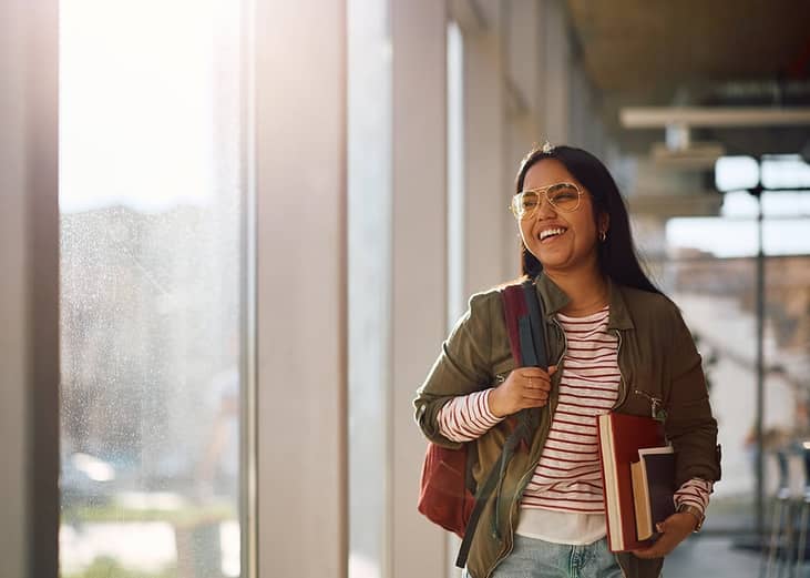 A smiling university student standing in the campus' hallway before her classes start.