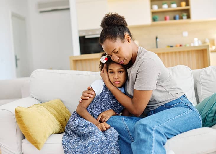 Mother embraces daughter on a couch at home while comforting her after a difficult day