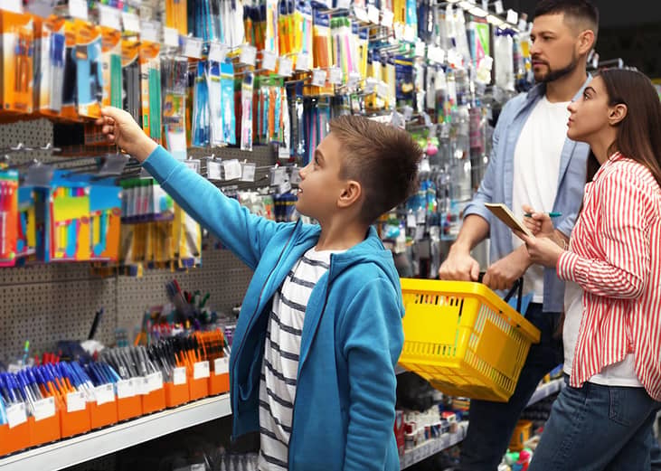 A young boy with his family choosing school supplies in the supermarket.