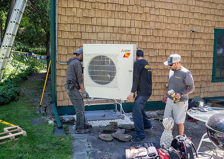 HVAC technicians prepare to install a condenser to a residential heat pump system.