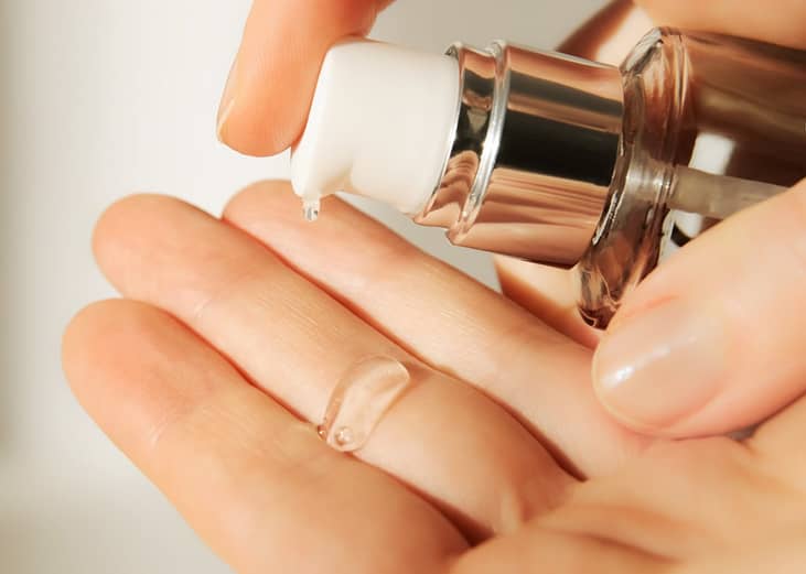 A cosmetologist squeezing out a moisturizing hyaluronic serum on her hand before a facial session.