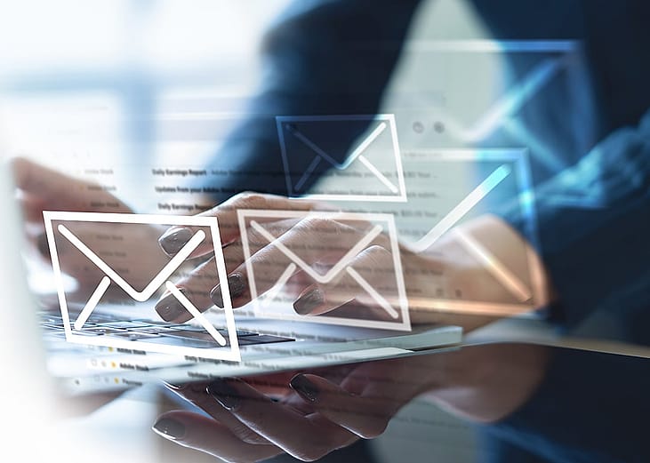 A digital overlay of envelope icons appearing over an office professional typing from a laptop, signifying email and newsletter updates.