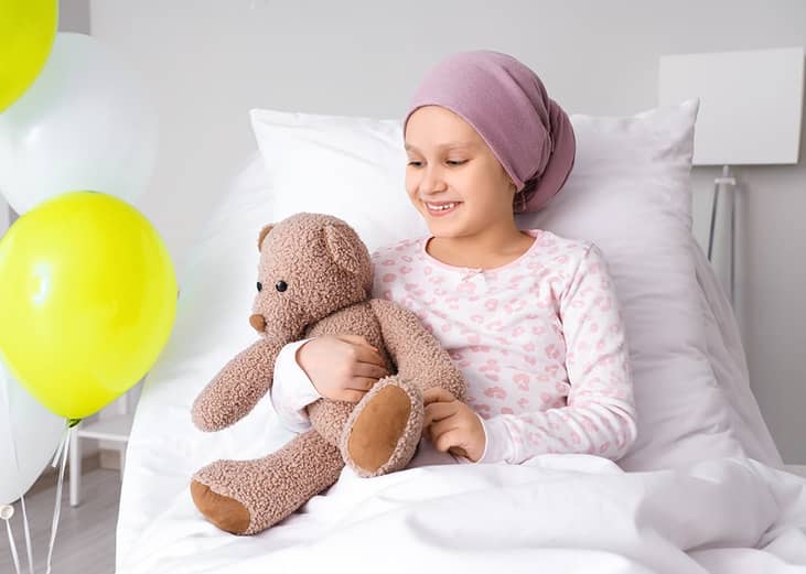 A young girl happily holding a teddy bear after chemotherapy.