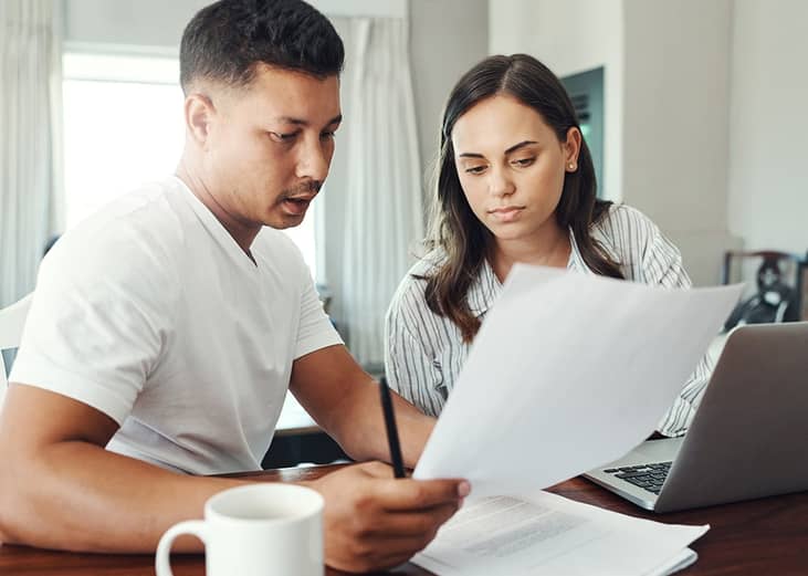 A married couple reviewing their family's financial documents and other paperwork for a loan refinancing.