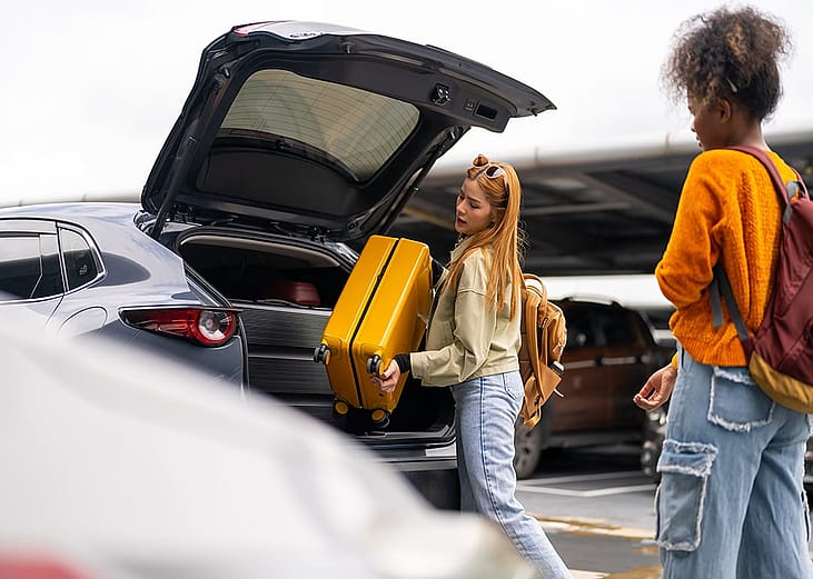 A person taking out her luggage from a car's trunk at an airport.