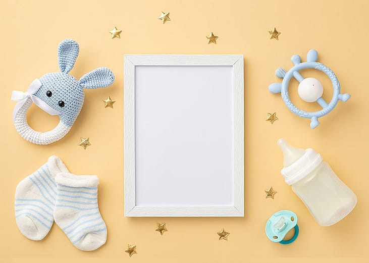 A blank photo frame placed in the center with baby accessories surrounding it in a pastel-colored background.