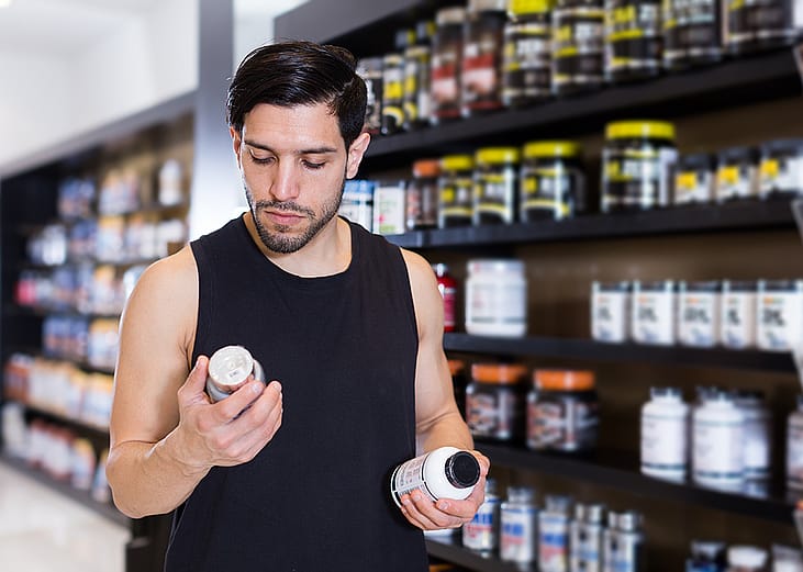 A young man carefully reading the label on a dietary supplement item at a store.