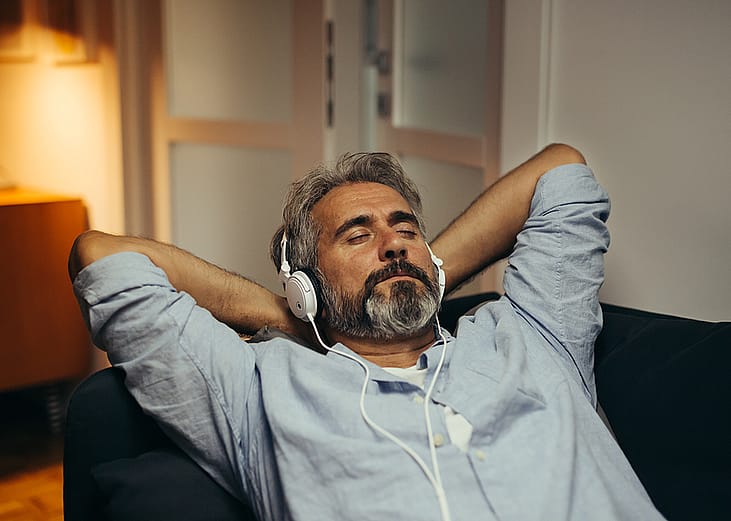A relaxed middle age man listening to music on the sofa.