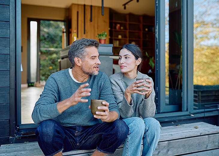 A couple talking and drinking coffee together outside their home.