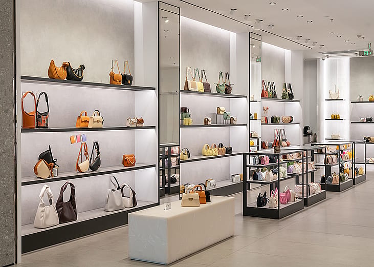 A modern luxury fashion store displaying handbags and purses in racks and tables at a shopping mall.