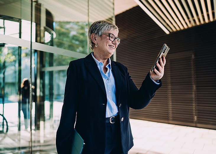 A senior businesswoman smiling at smartphone screen.