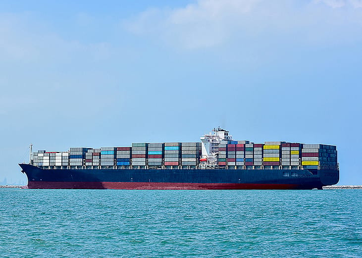 A huge container cargo ship sailing in the open sea under a cloudy sky.