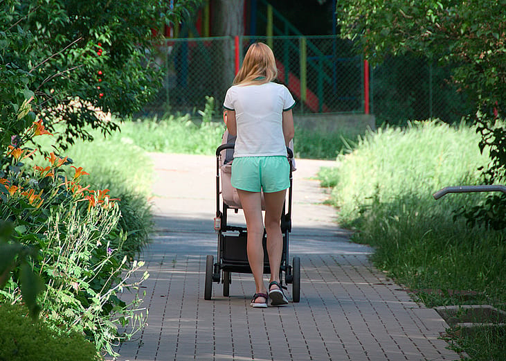 Rear view of a young mother pushing her baby's stroller while taking them on a walk.