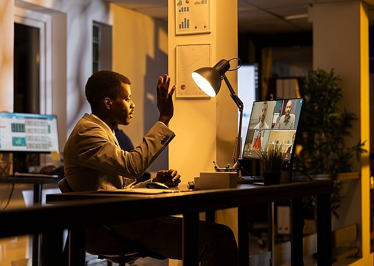 A professional interacting in an online conference with remote participants at his home office.