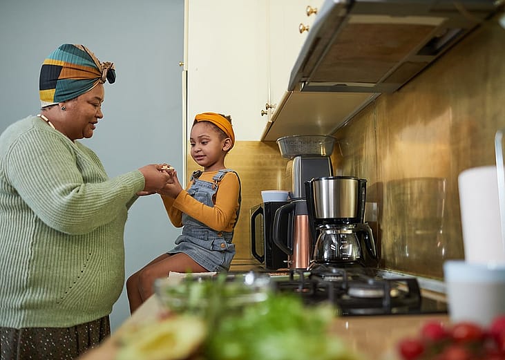 A grandmother with her granddaughter sharing a snack in their home kitchen.