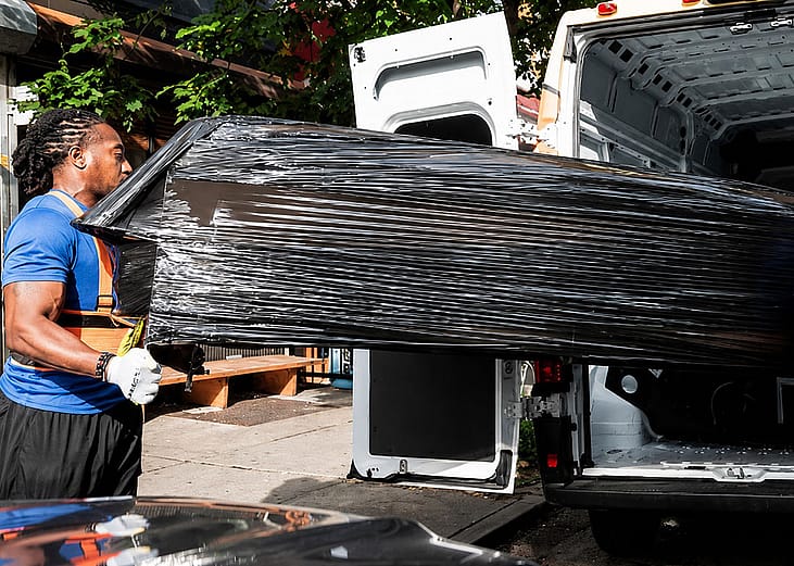 A professional mover loading a large and heavy-wrapped furniture into a delivery van.