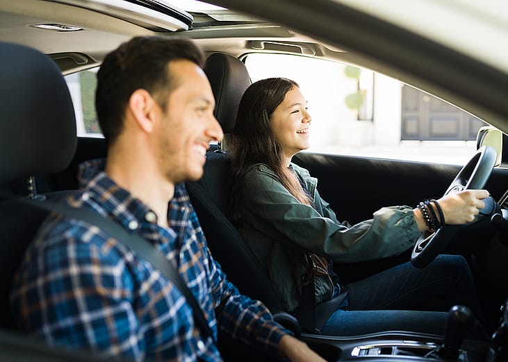 A father guiding her teenage daughter on how to drive.