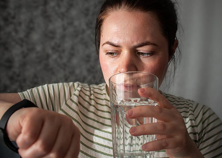A person checking her heart rate and pulse from a smart watch, while drinking a glass of water.