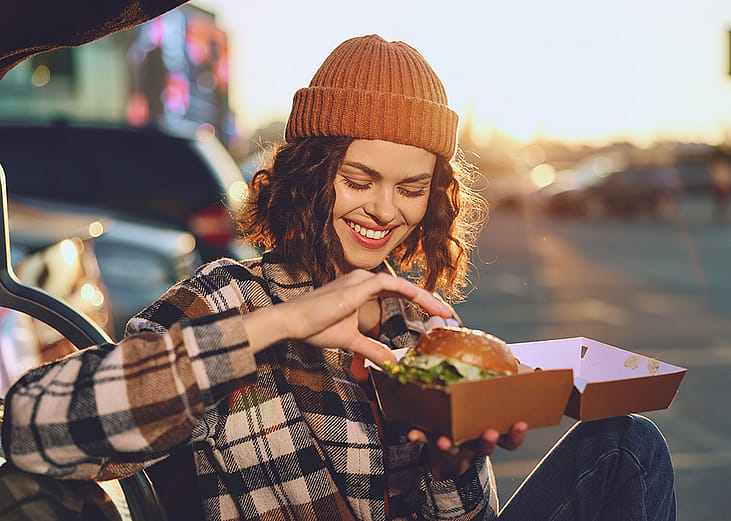 A young woman happily eating a takeout burger.