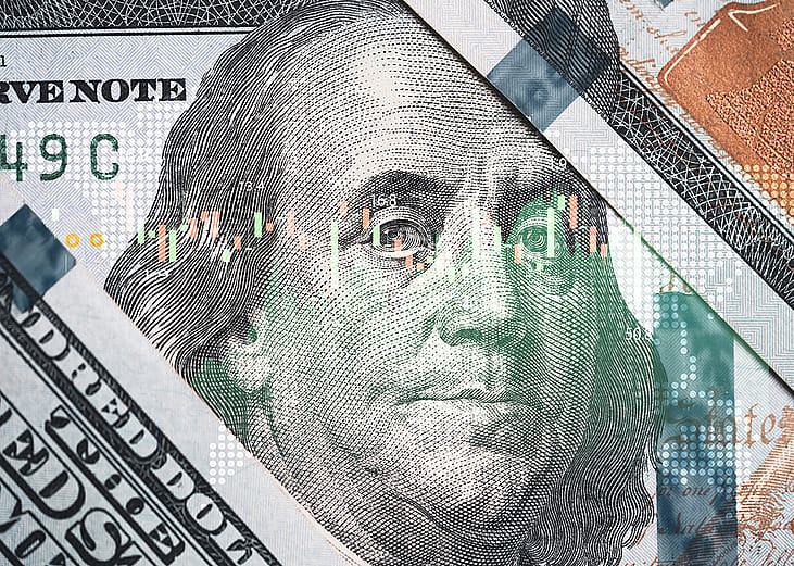 A close-up of Benjamin Franklin's face on a U.S. 100-dollar bill overlaid with a stock market trading chart.