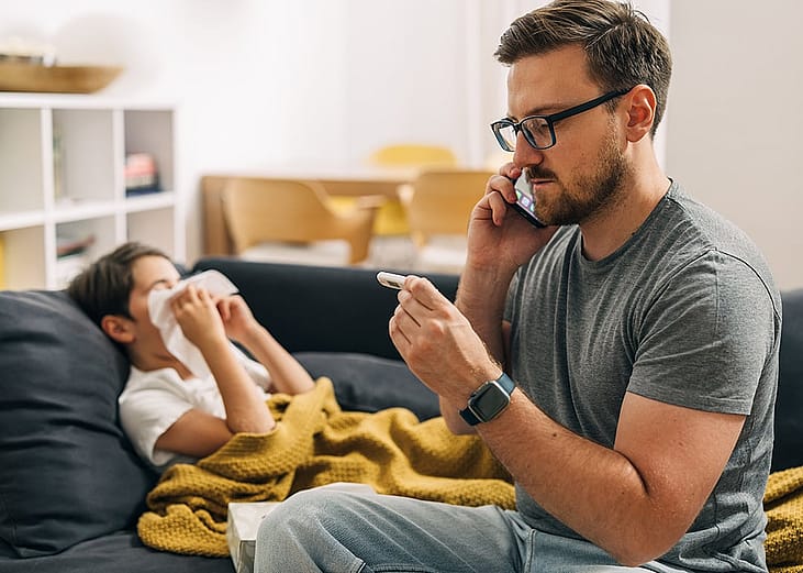 A parent calling a pediatrician over the phone, while checking his child's body temperature due to the flu.
