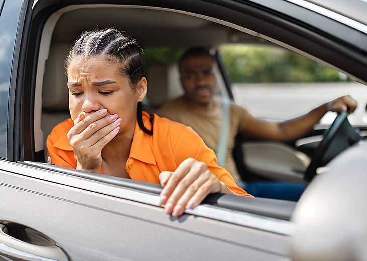 A person feeling nauseous and leaning out of the car's window during a quick stop.