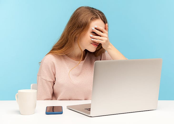 A nervous employee looking at her laptop through her fingers.
