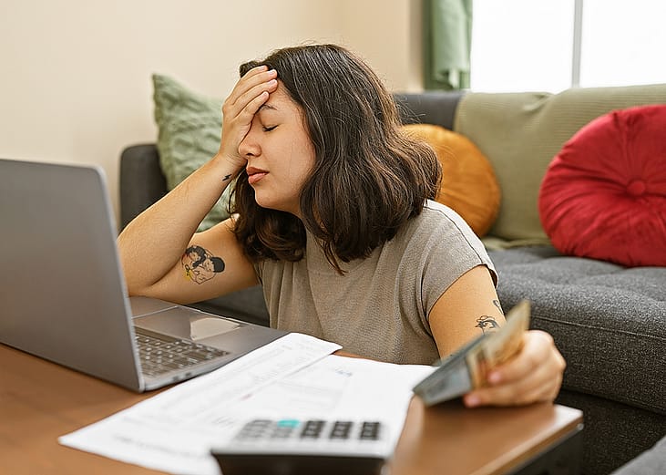 An overwhelmed young woman at home reviewing documents.