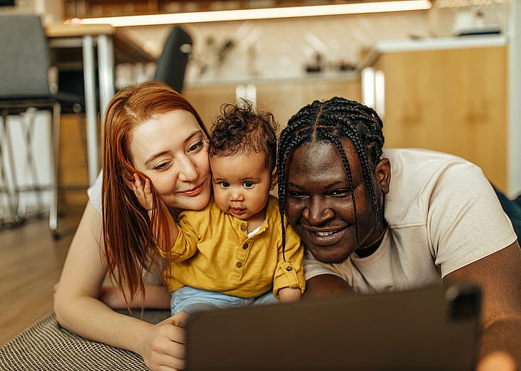 A happy couple with their young child watching something from a digital tablet.