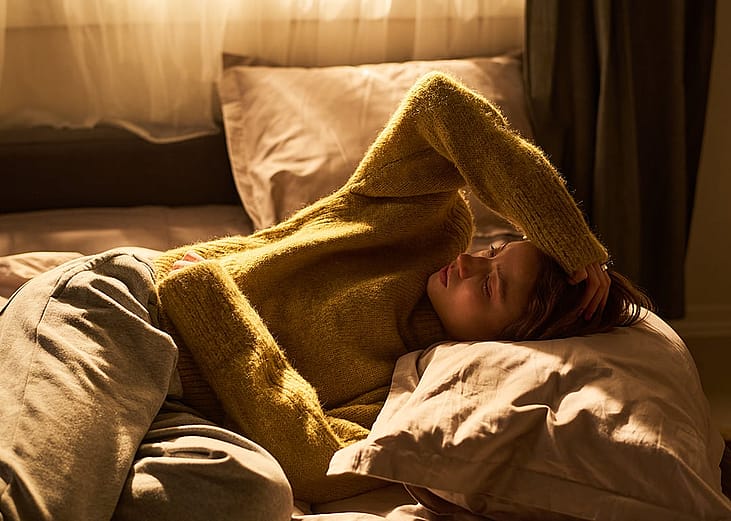 Young woman lying in bed at home experiencing discomfort.