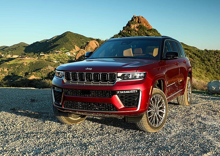 Front view of a red 2026 Jeep Grand Cherokee parked on dirt road with hills in the background.