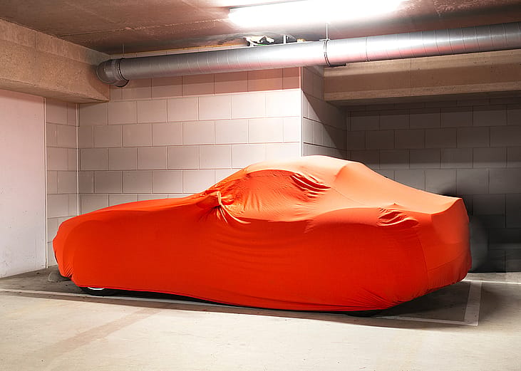 A modern luxury car with an orange-colored protection cover parked in a basement garage.