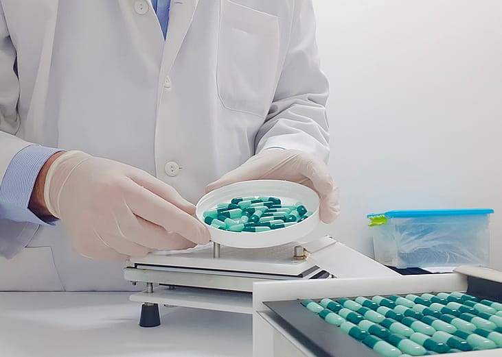 A specialized pharmacist using a manual filling machine to compound medicine capsules in a laboratory.